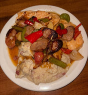 Plated dish with chicken, sausage, and vegetables on a white plate.