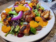 A plate of Nona's Salad with Blackened Shrimp, featuring mixed greens, raisins, grapes, mandarin oranges, red onion, and blackened shrimp pieces, all dressed in a citrus vinaigrette.