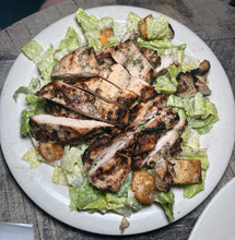 Grilled chicken salad with lettuce and croutons on a white plate.
