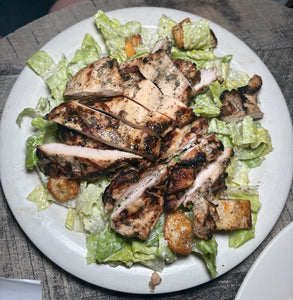 Grilled chicken salad with lettuce and croutons on a white plate.