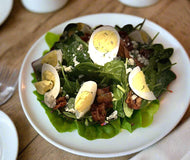 A plate of Spinach Salad with hard boiled eggs, bacon, and blue cheese crumbles tossed in a vinaigrette dressing.