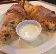 A plate with a buffalo chicken roll served with bleu cheese dressing on the side, the roll appears golden brown with a crispy crust and a small container of white sauce for dipping.
