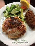 A plate containing stuffed cod fish, served with a side of vegetables and a choice of potato or rice. A lemon wedge is also present on the plate.
